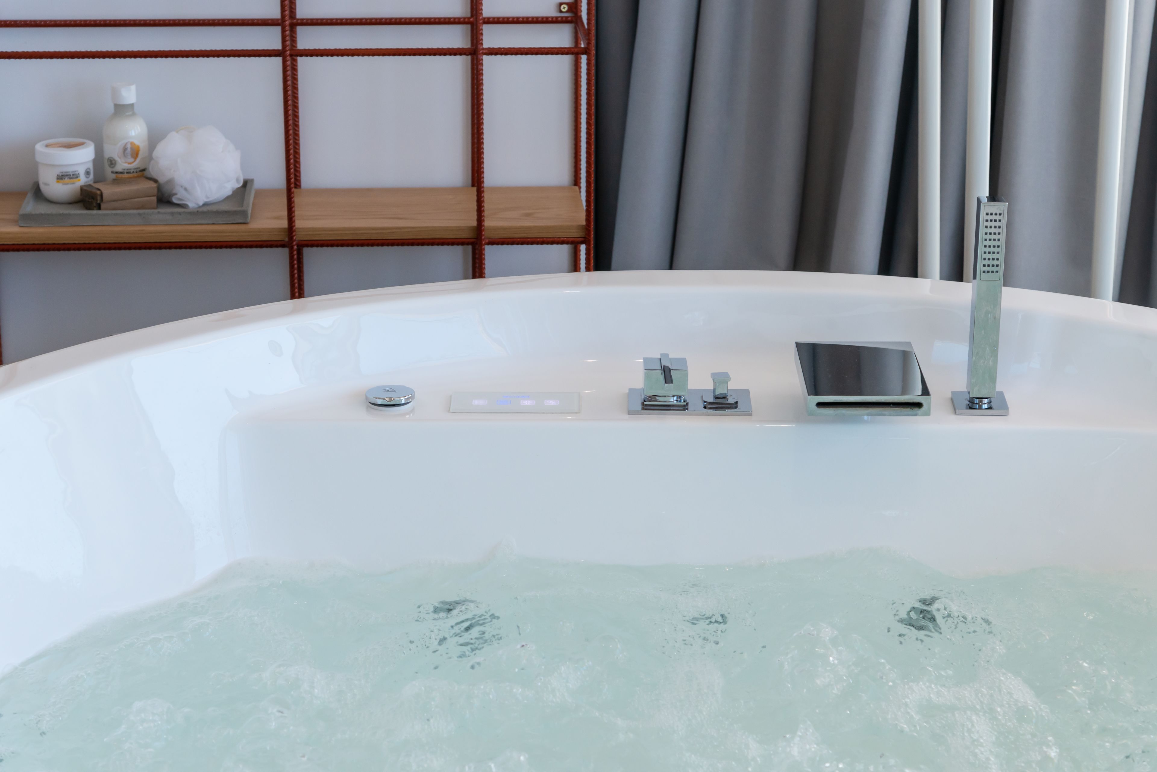 Une salle de bain moderne avec une baignoire, un panneau de commande et une étagère contenant des articles de toilette.