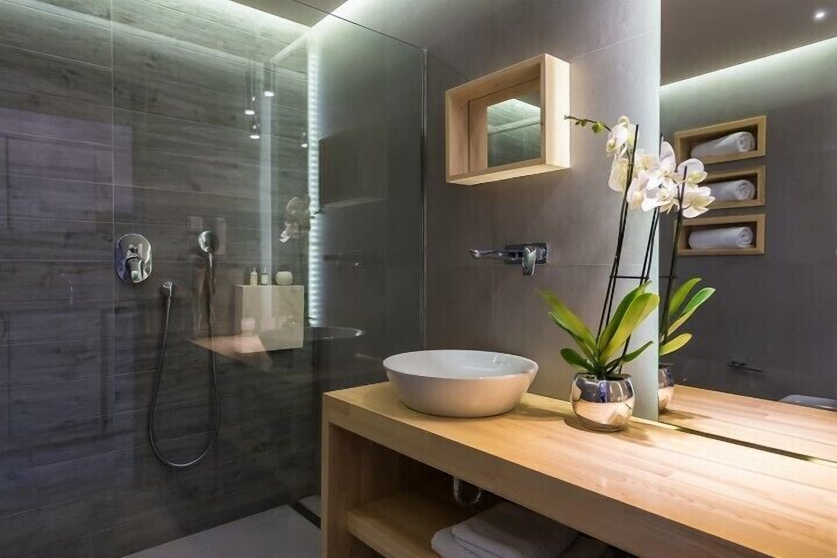 A modern bathroom with a glass shower enclosure, a wooden vanity with a large basin, and a mirror above it.