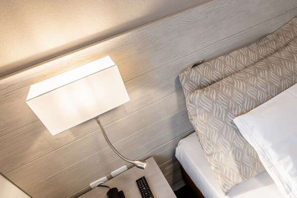 A neatly made bed with patterned bedding, a bedside table with a remote control, and a wall-mounted light fixture.