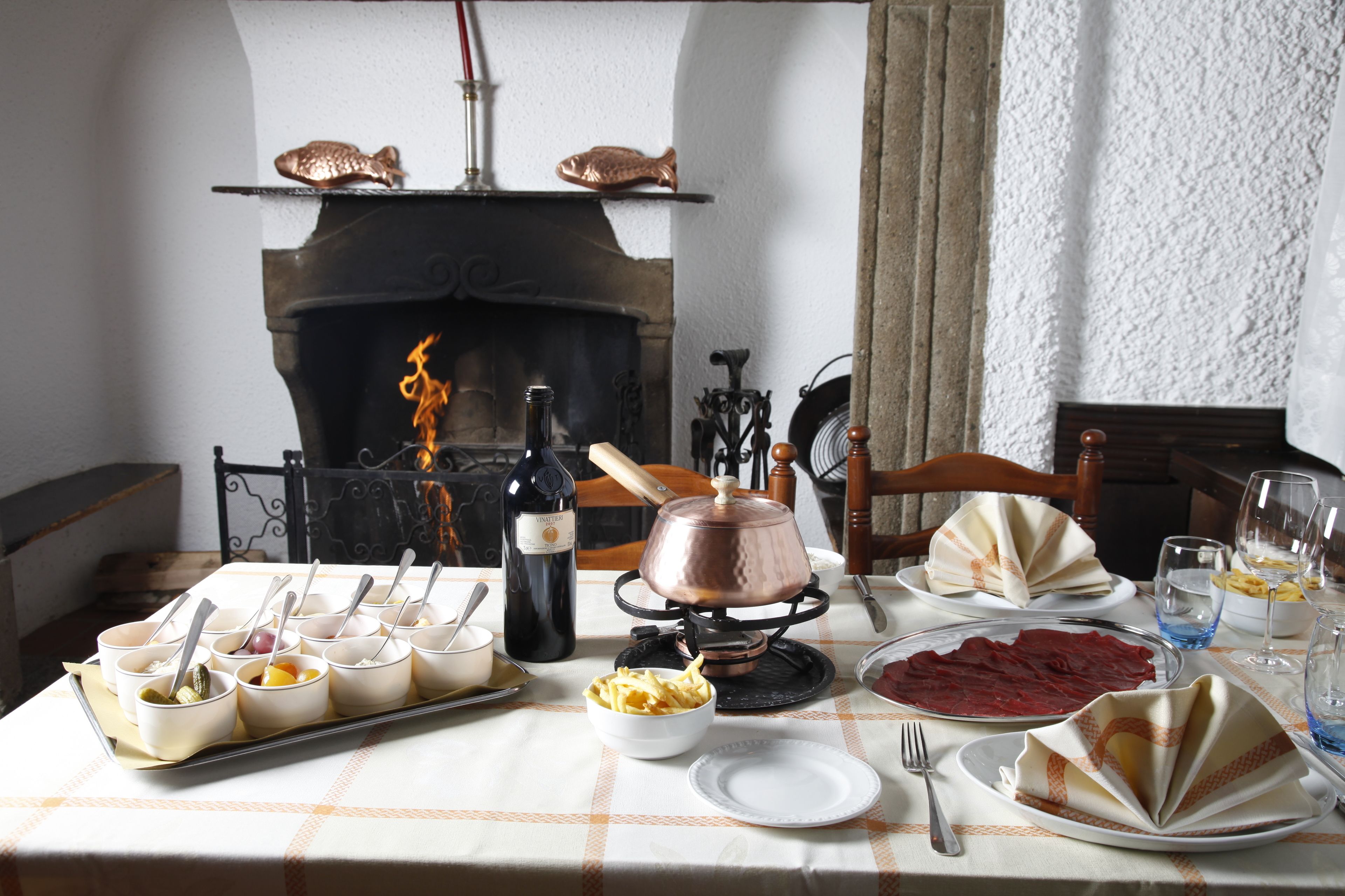 Un tavolo da pranzo apparecchiato con diversi piatti, una bottiglia di vino e un camino sullo sfondo.
