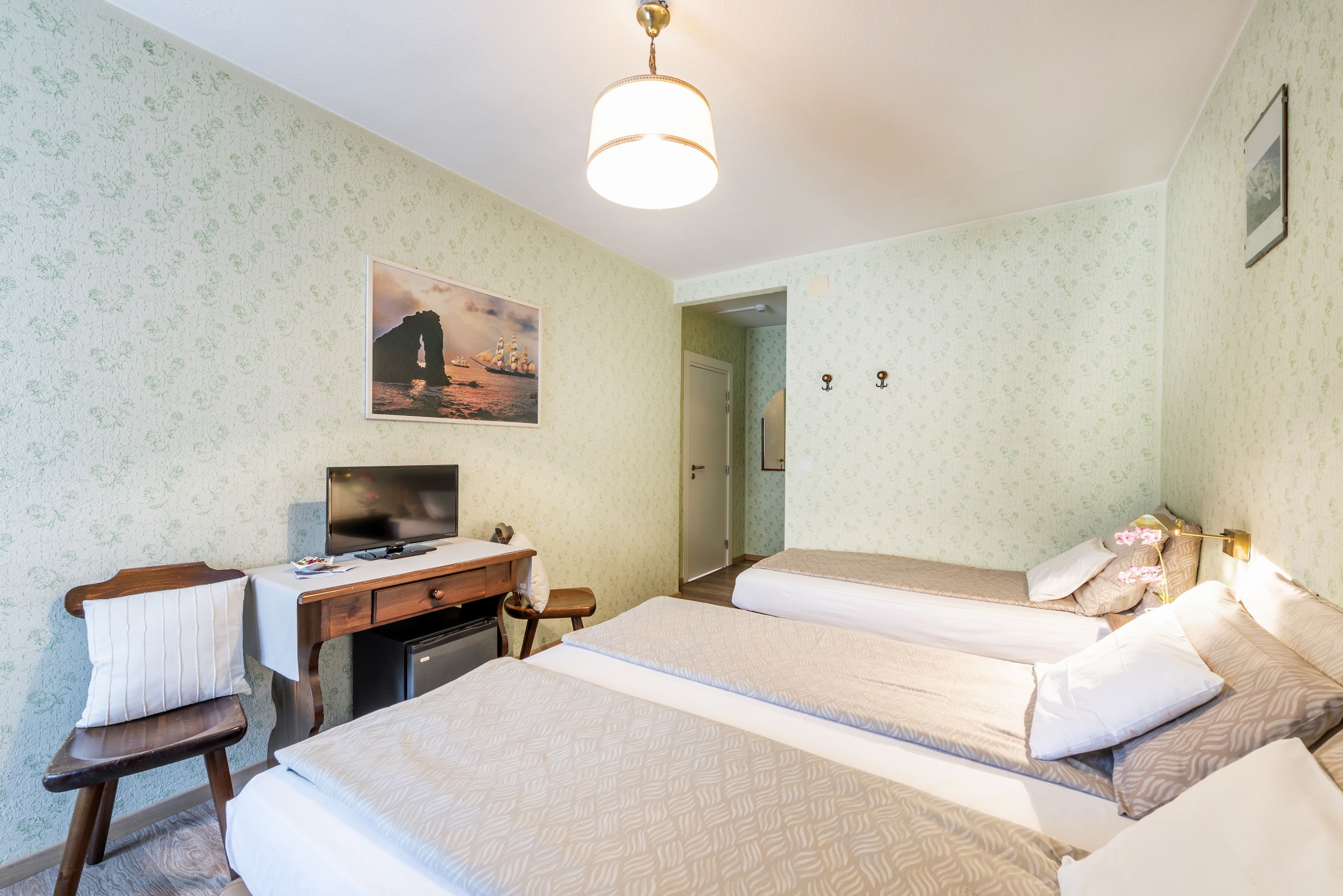 Una camera d'albergo con due letti, una scrivania con televisore, una sedia e una porta che dà su un'altra stanza.