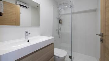 Un baño moderno con ducha de vidrio, lavamanos blanco y retrete.