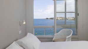 A bedroom with a large window offering a view of the sea and a distant shoreline. - Apartamentos Rotilio (Sanxenxo)