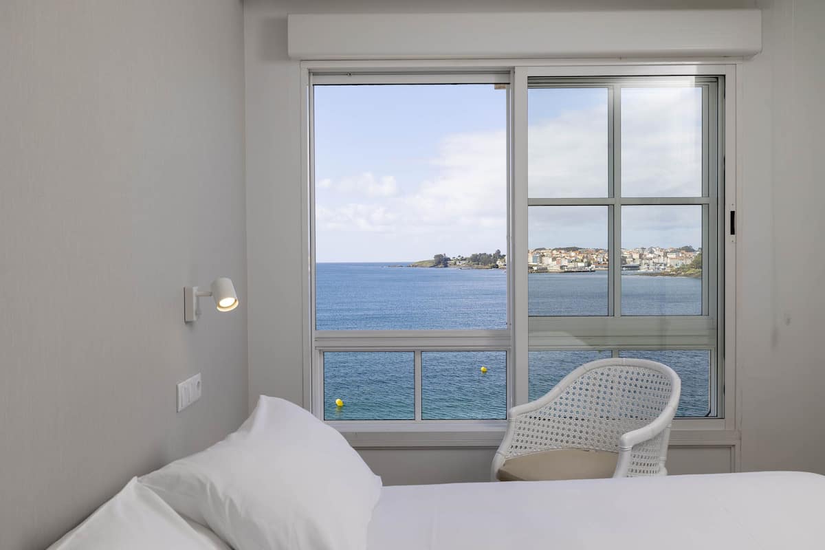 Quarto com uma janela grande que oferece vista para o mar e a costa distante.