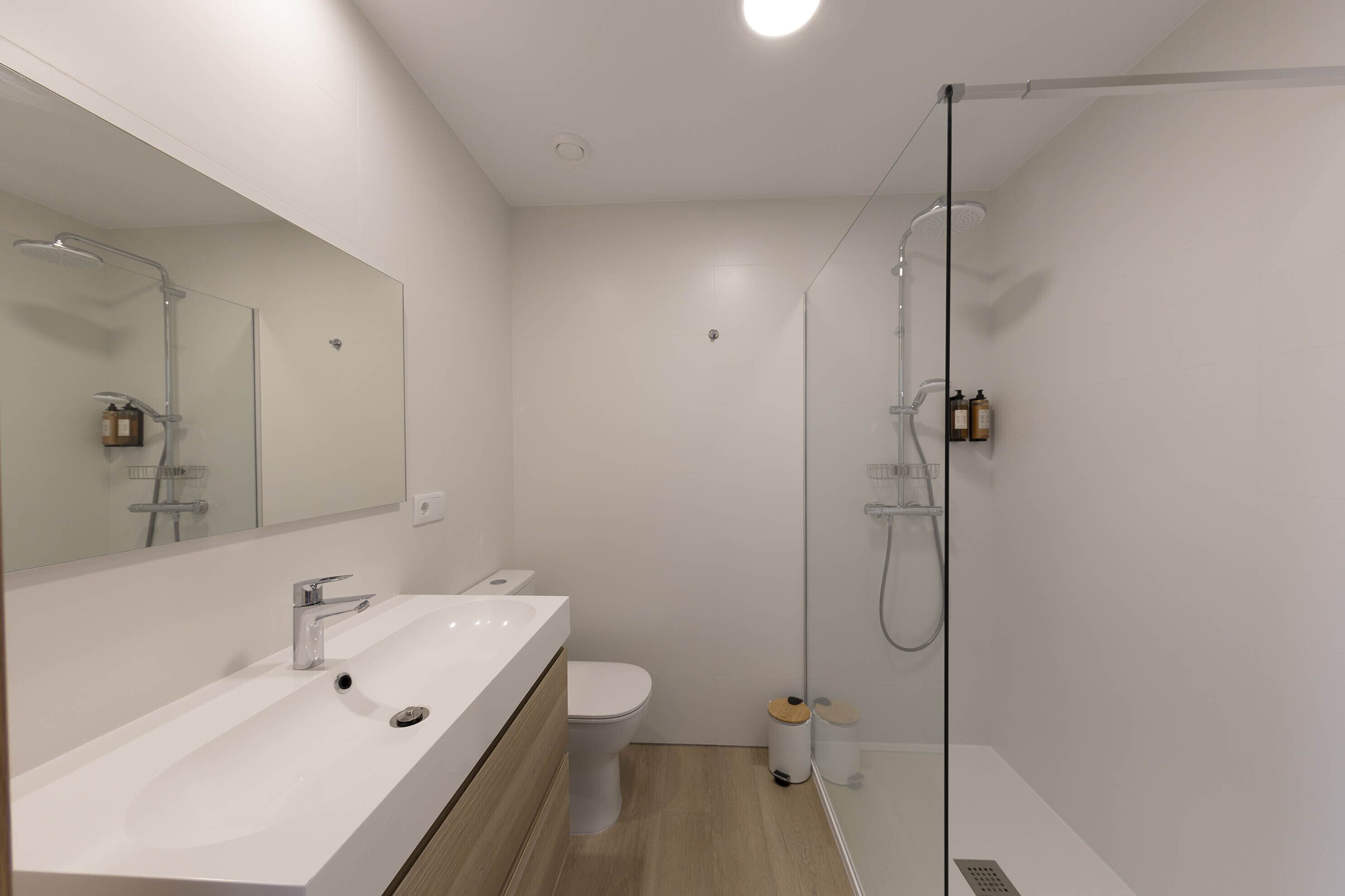 Un baño moderno con un lavamanos blanco, un inodoro y una zona de ducha con mampara de vidrio.