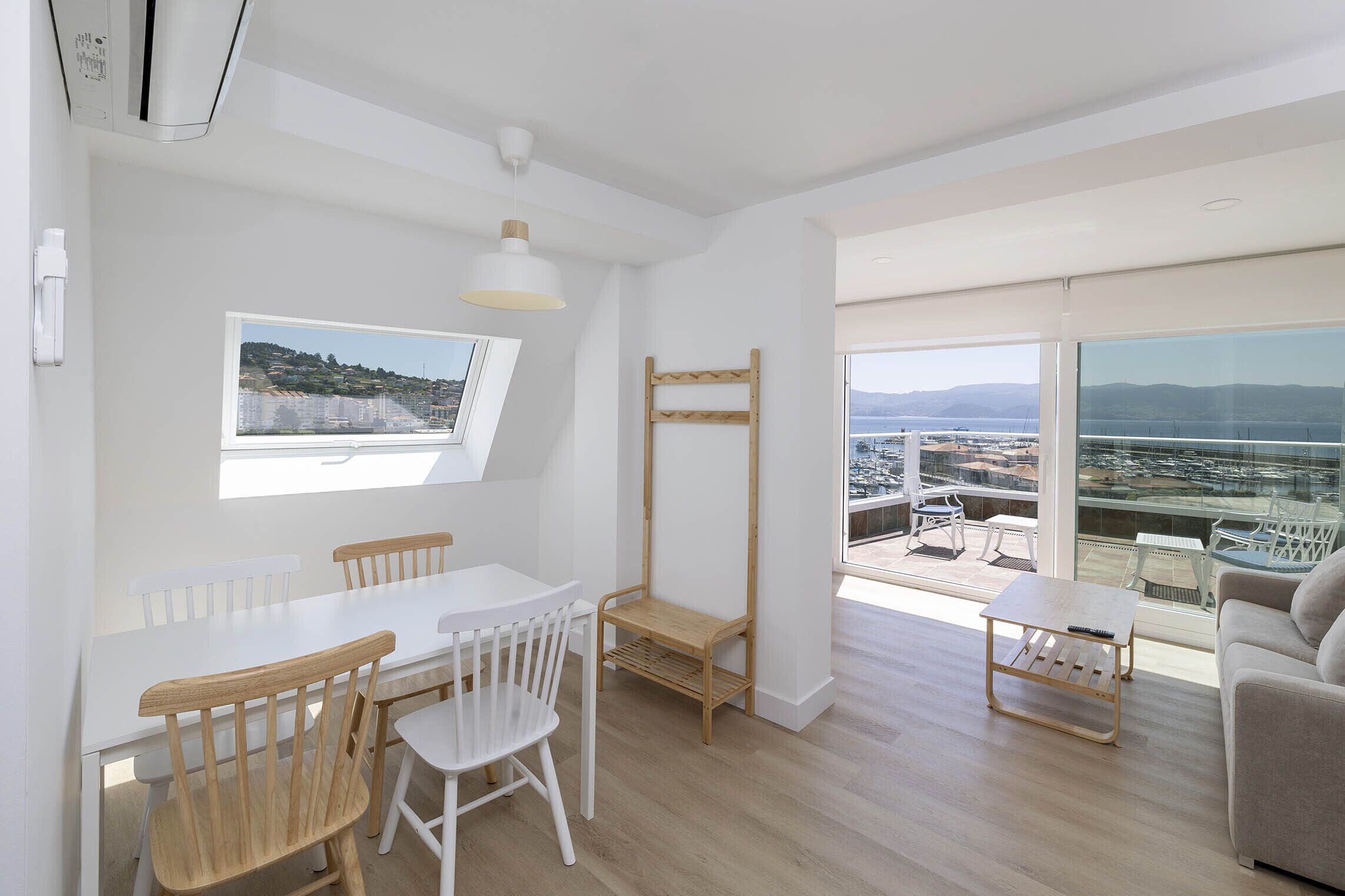 Una sala moderna con comedor, ventanas amplias con vista a la ciudad y un balcón con mobiliario exterior.