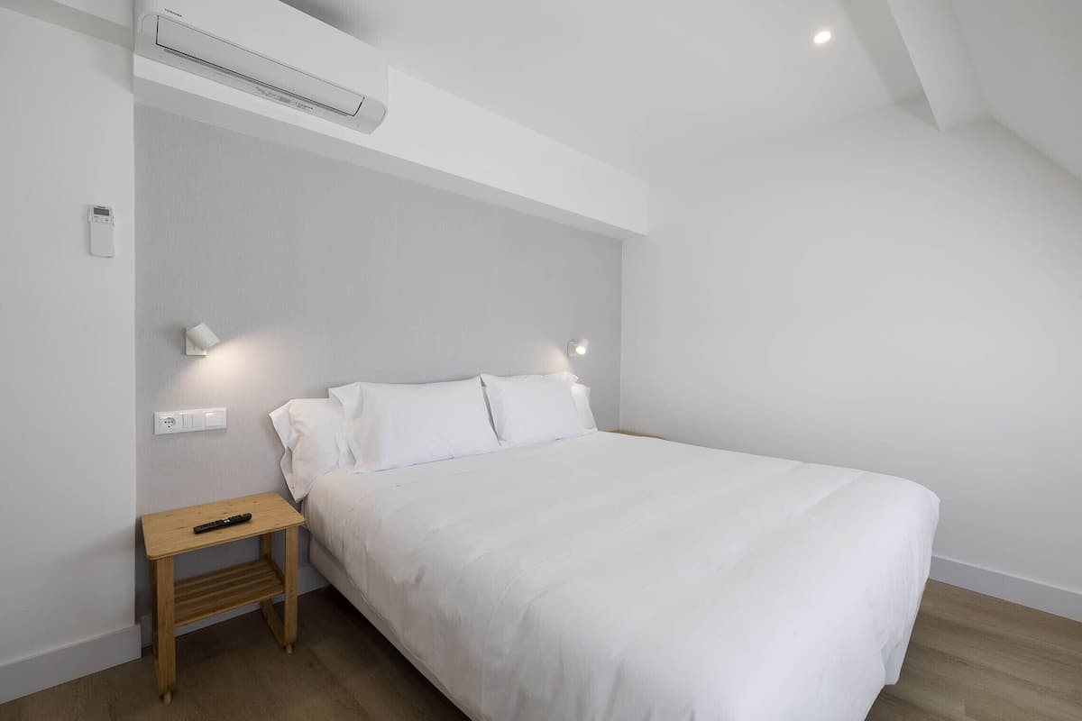 Quarto com cama, mesa de cabeceira, luminária na parede e aparelho de ar condicionado.