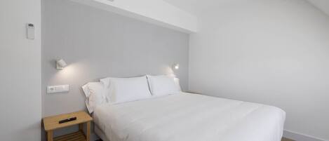Un dormitorio con cama, mesita de noche, lámpara de pared y equipo de aire acondicionado.