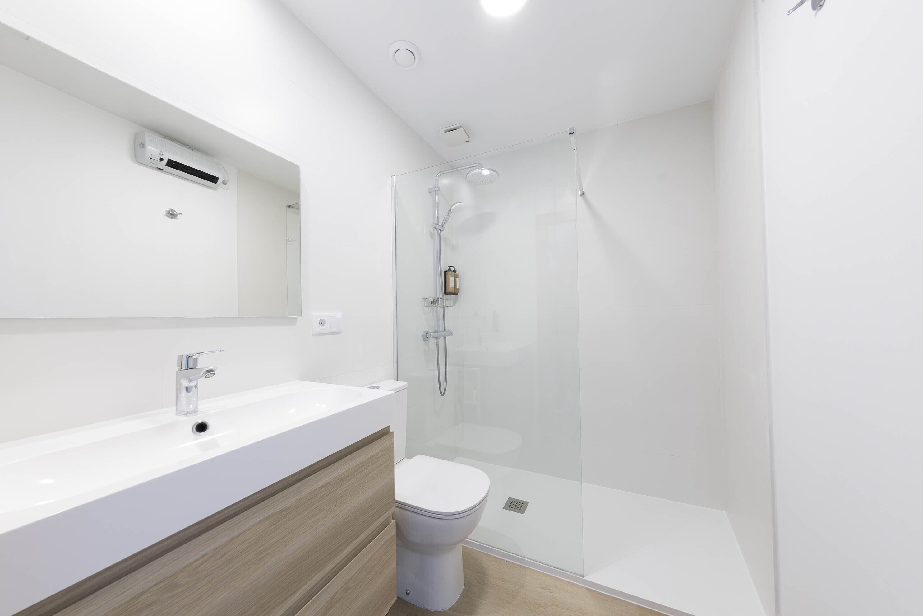 Un baño moderno con lavamanos blanco, tocador de madera y ducha con mampara de vidrio.