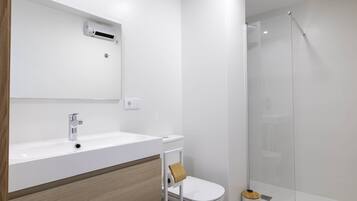 Un bany modern amb un lavabo blanc, un vàter i una dutxa amb envàs de vidre.