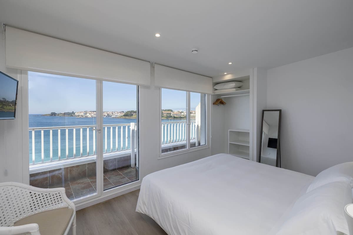 Quarto com uma cama grande, uma cadeira e vista para o mar através de uma varanda.