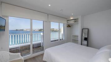 Un dormitorio con una cama grande, una silla y vista al mar desde un balcón.