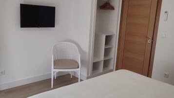 Un dormitorio con una cama, una silla blanca, un armario y un televisor montado.