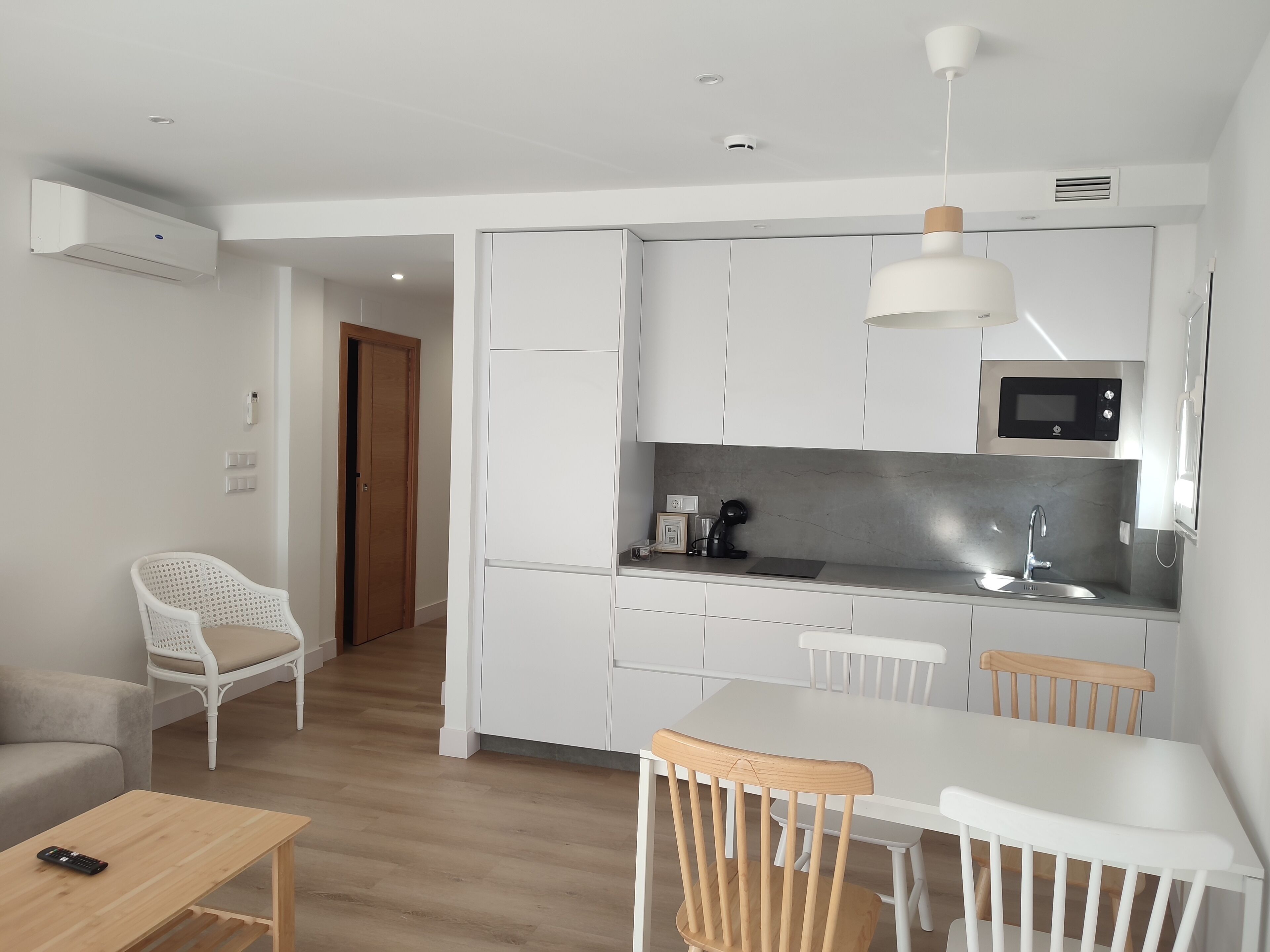 A modern kitchen with white cabinets, a microwave, and a sink. There is a dining area with a table and chairs.