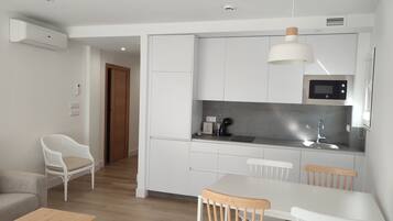 A modern kitchen with white cabinets, a microwave, and a sink. There is a dining area with a table and chairs.