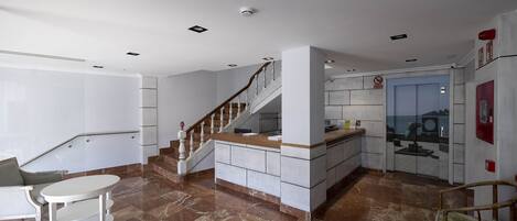 A modern kitchen with a marble floor, a wooden staircase, and a view of the city through a glass door.
