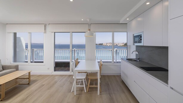 A modern kitchen with a large window, a dining area, and a view of the sea. - Apartamentos Rotilio (Sanxenxo)