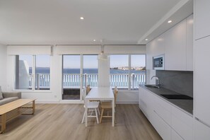 A modern kitchen with a large window, a dining area, and a view of the sea. - Apartamentos Rotilio (Sanxenxo)