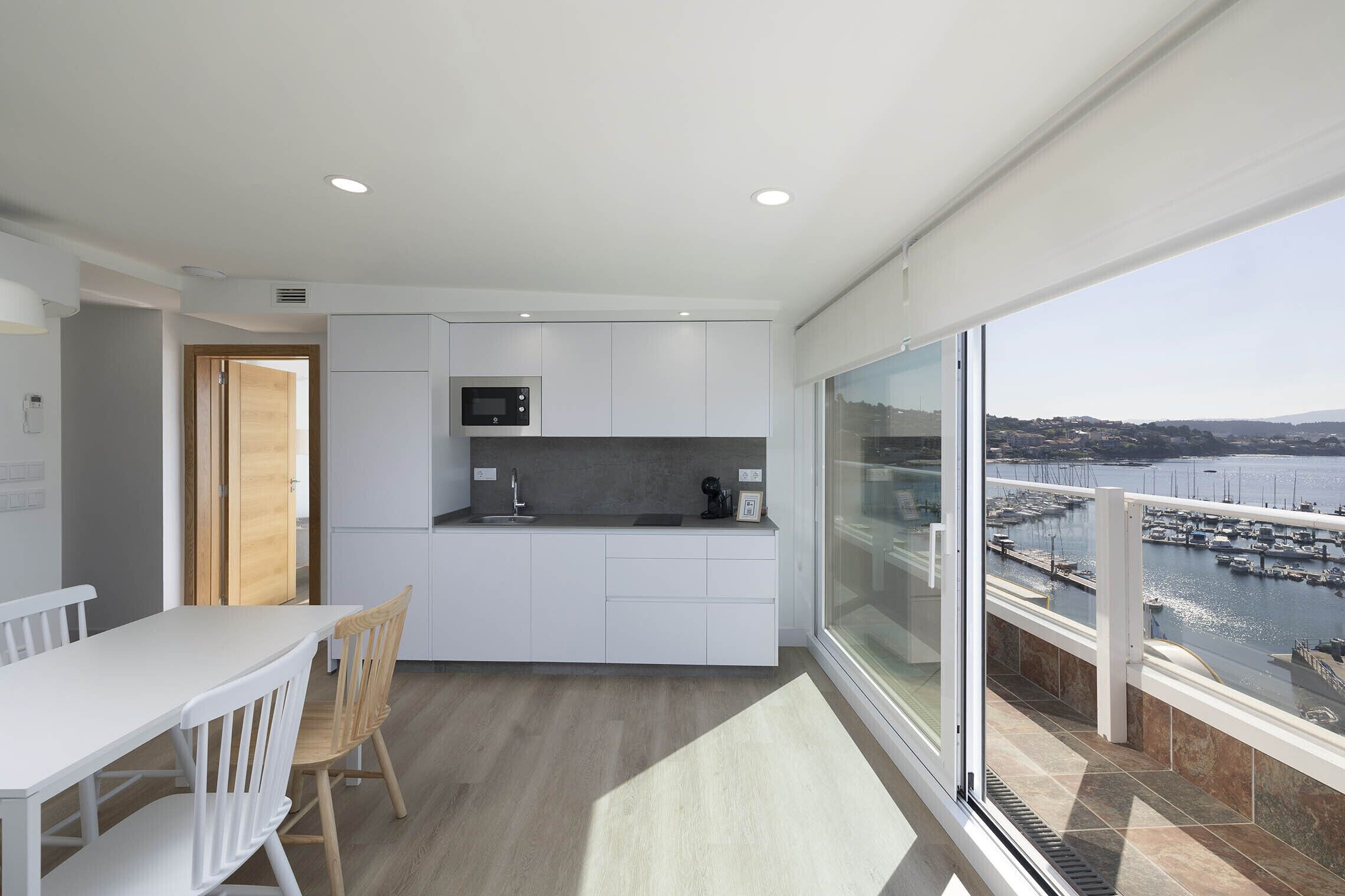 A modern kitchen with white cabinetry, a microwave, and a view of a marina through large windows.