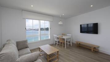 Una sala de estar moderna con un ventanal grande, un sofá, una mesa de madera, un juego de comedor y un televisor montado en la pared.