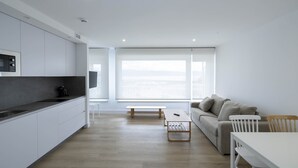 A modern, minimalist living space with a kitchen, dining area, and seating by a large window. - Apartamentos Rotilio (Sanxenxo)