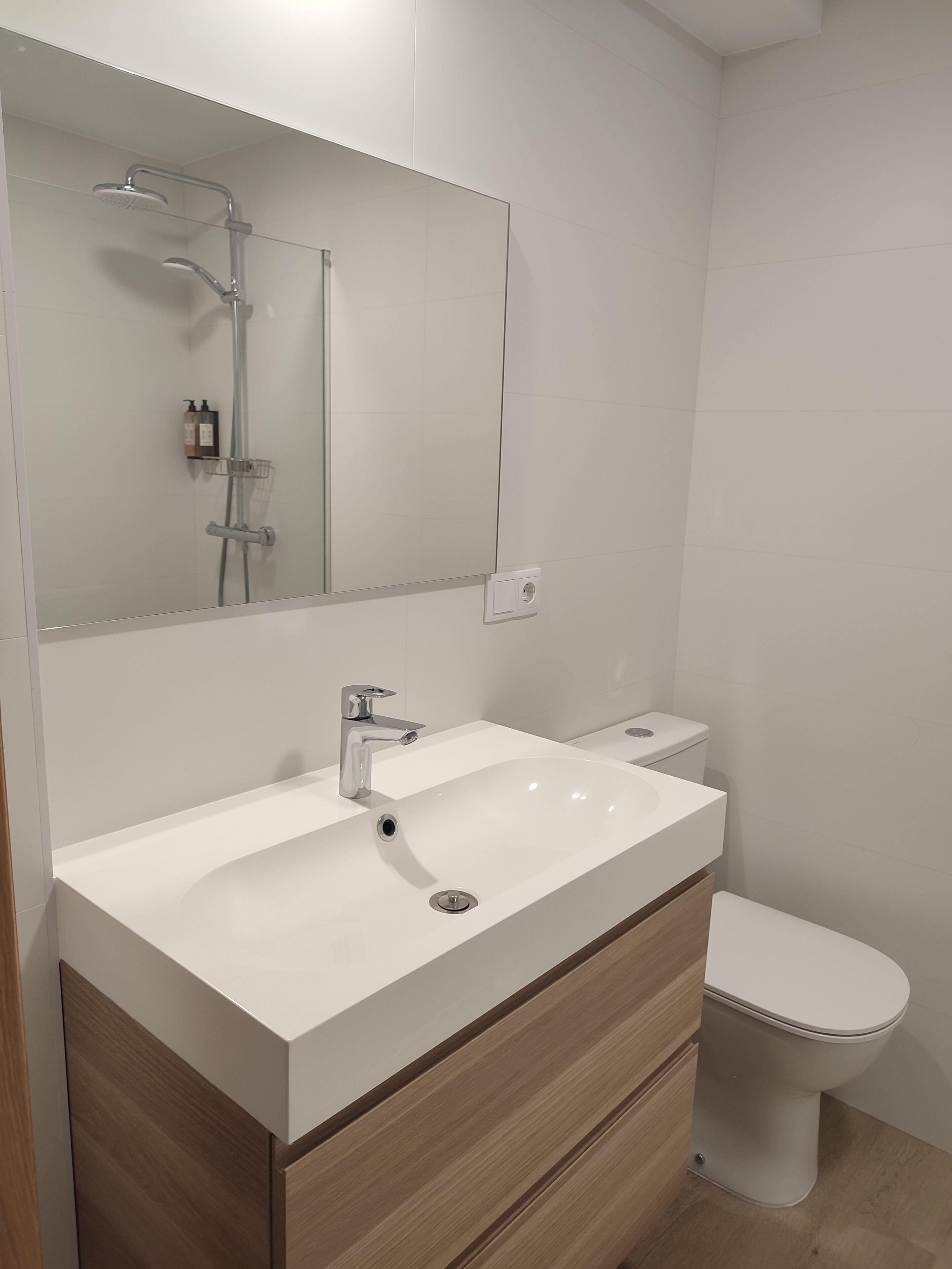 A modern bathroom with a white sink, a mirror, a shower, and a toilet.