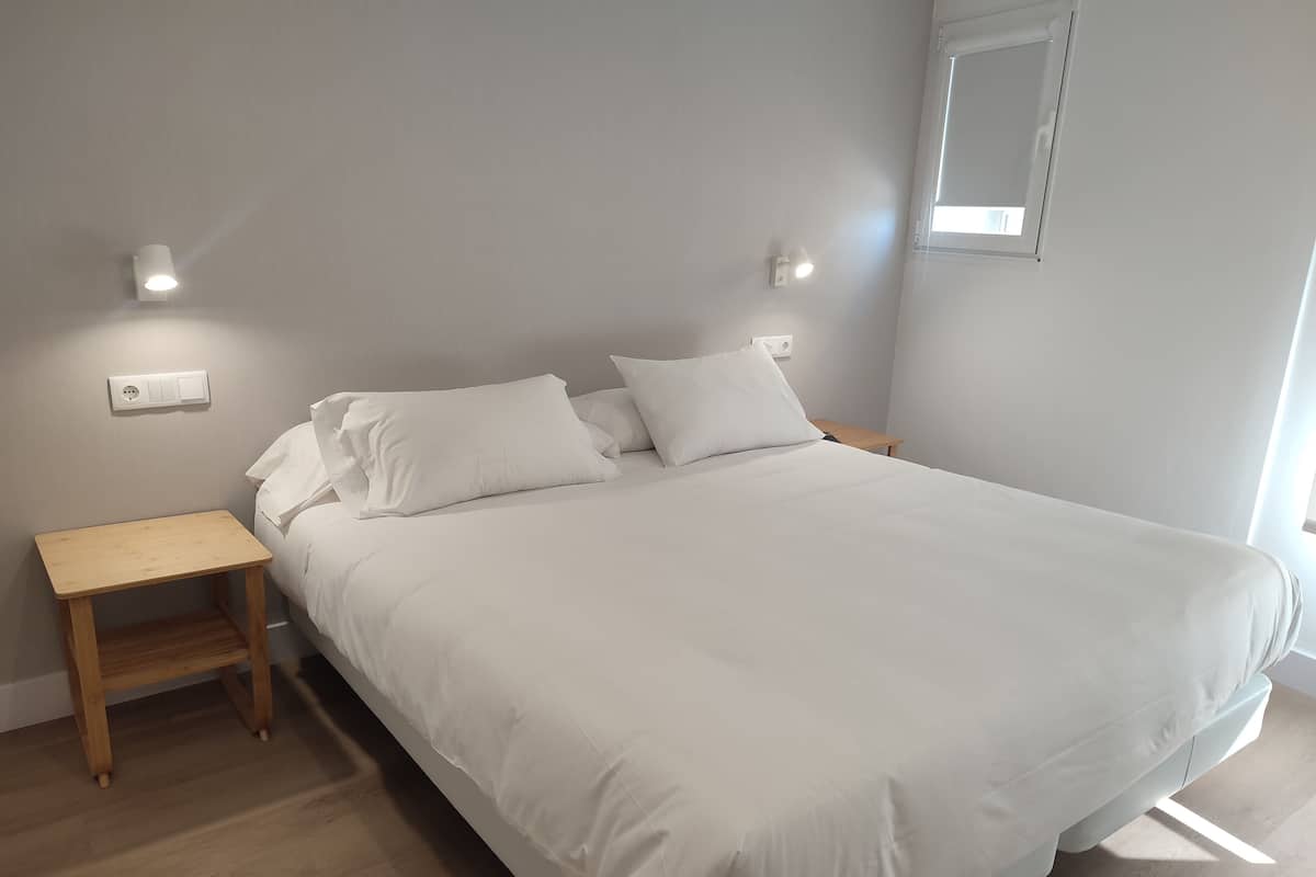 Quarto com cama, mesa de cabeceira e luminária na parede.
