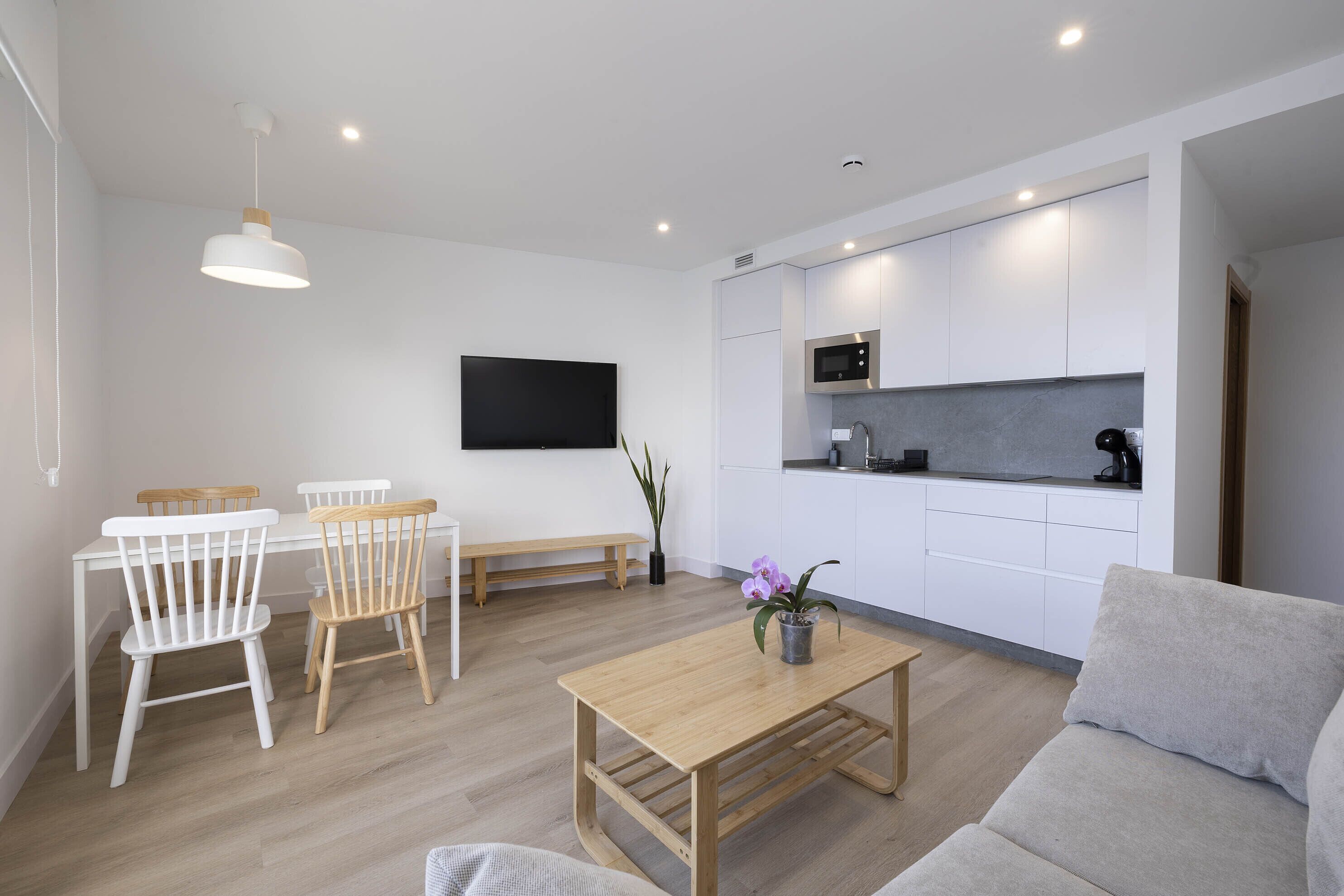 Una sala de estar moderna con una mesa de centro de madera, un sofá gris y un comedor con sillas blancas y un banco.