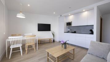 Una sala de estar moderna con una mesa de centro de madera, un sofá gris y un comedor con sillas blancas y un banco.