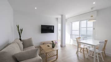 A modern living room with a sofa, a wooden table, and a dining area with chairs.