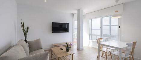 A modern living room with a sofa, a wooden table, and a dining area with chairs.