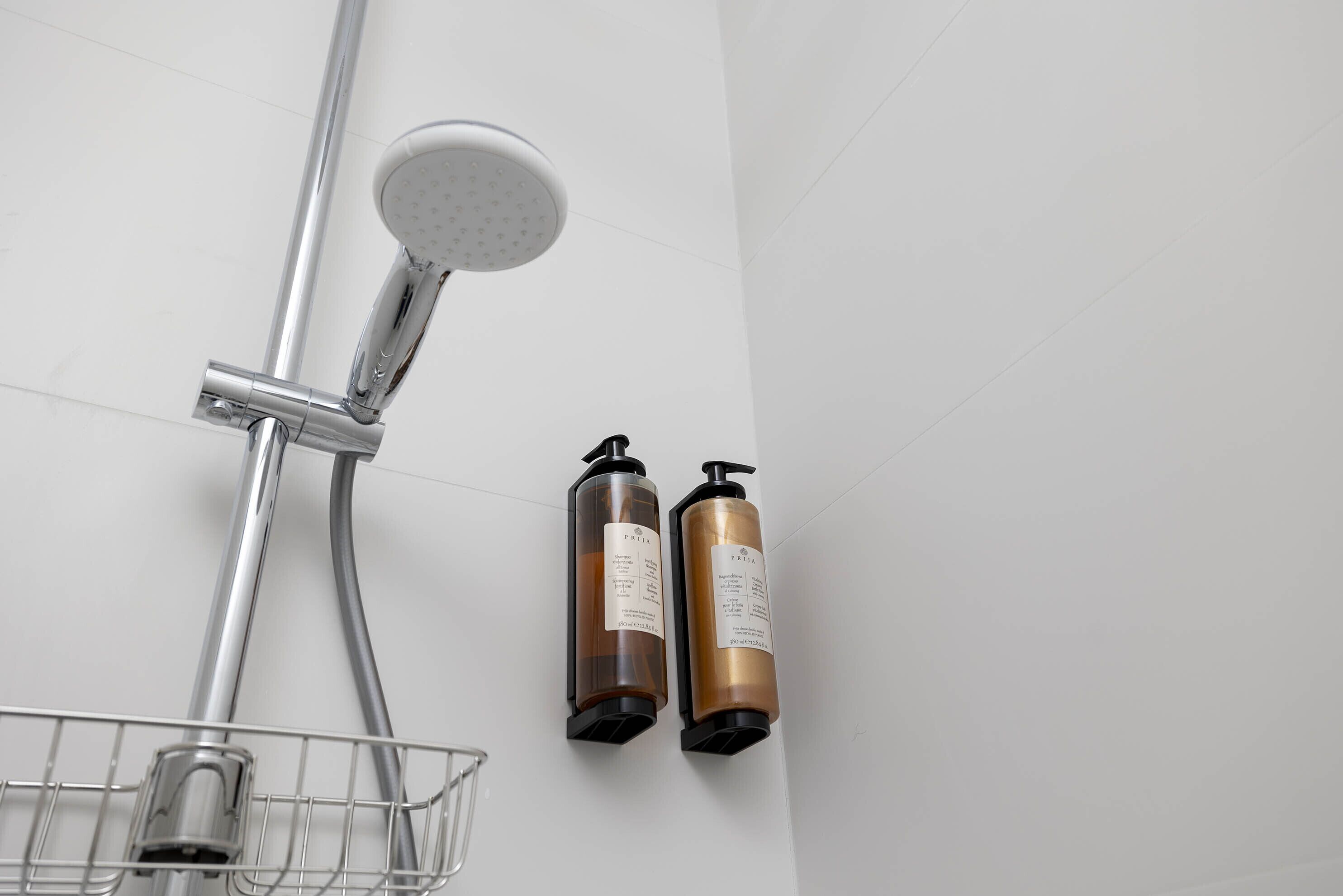Ducha con cabezal de ducha manual, grifo empotrado en la pared y dos botellas de champú y acondicionador.