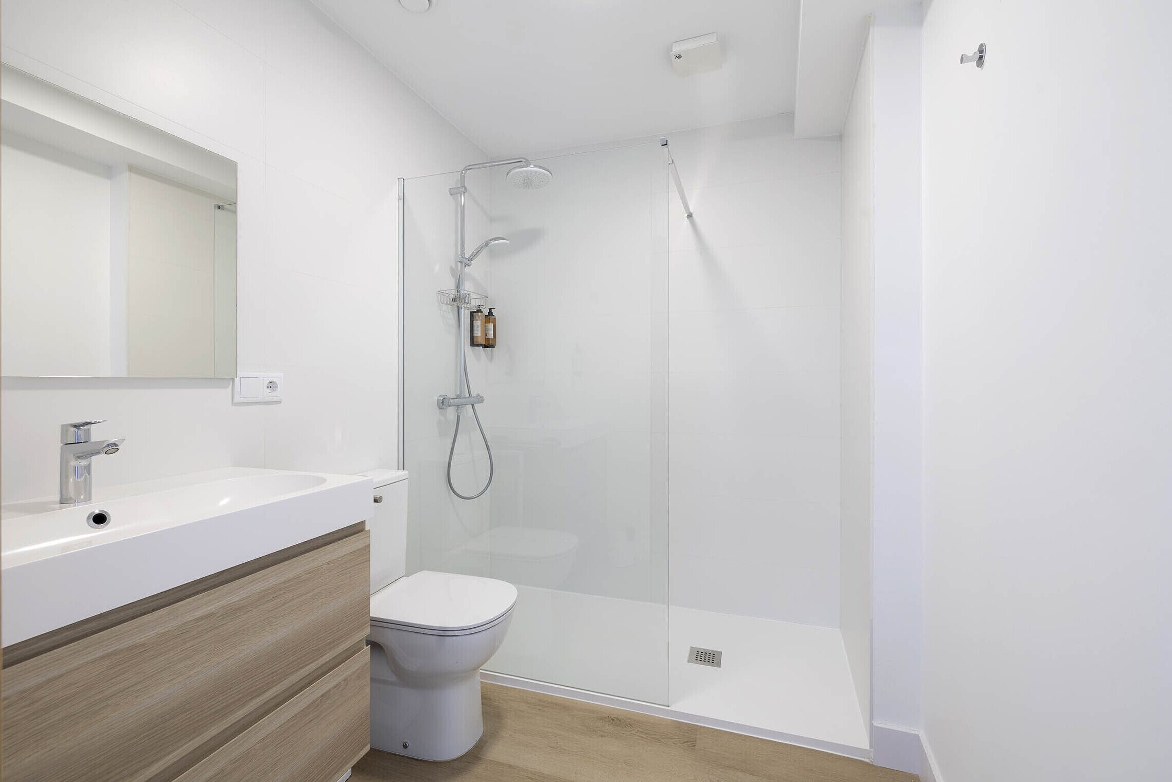 A modern bathroom with a white sink, mirror, and toilet, and a glass-enclosed shower area.