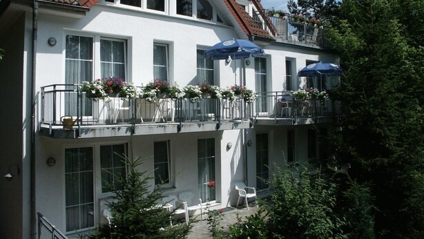A two-story building with a white facade, multiple balconies with flower boxes, and outdoor seating. - Waldhaus Mühlenbeck (Mühlenbecker Land)