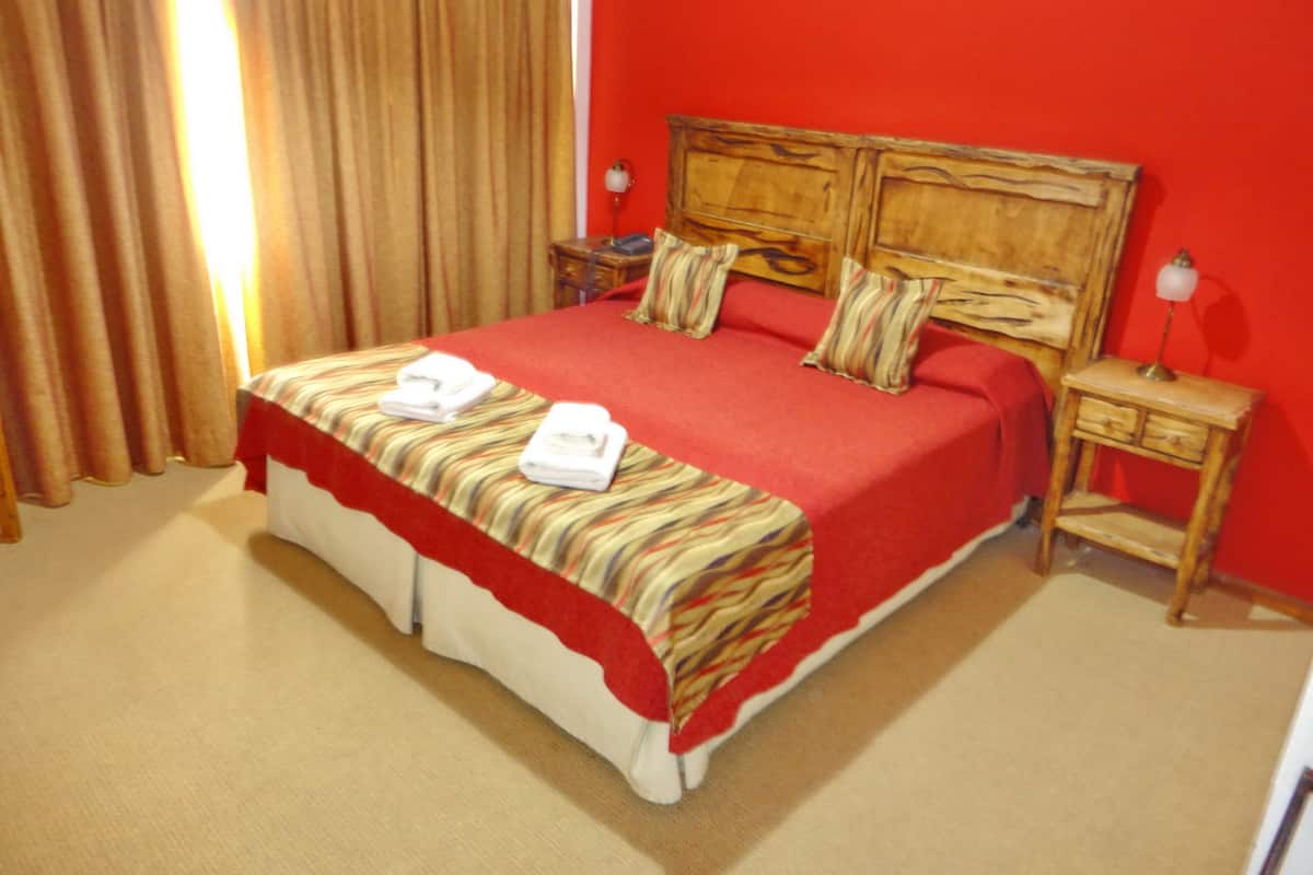 A hotel room with a large bed, red walls, a wooden headboard, two bedside tables, and a red and white striped bedspread.