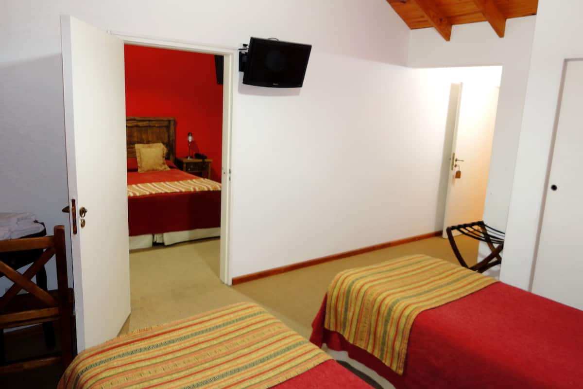 A room with two beds, a television mounted on the wall, and a door leading to another room.