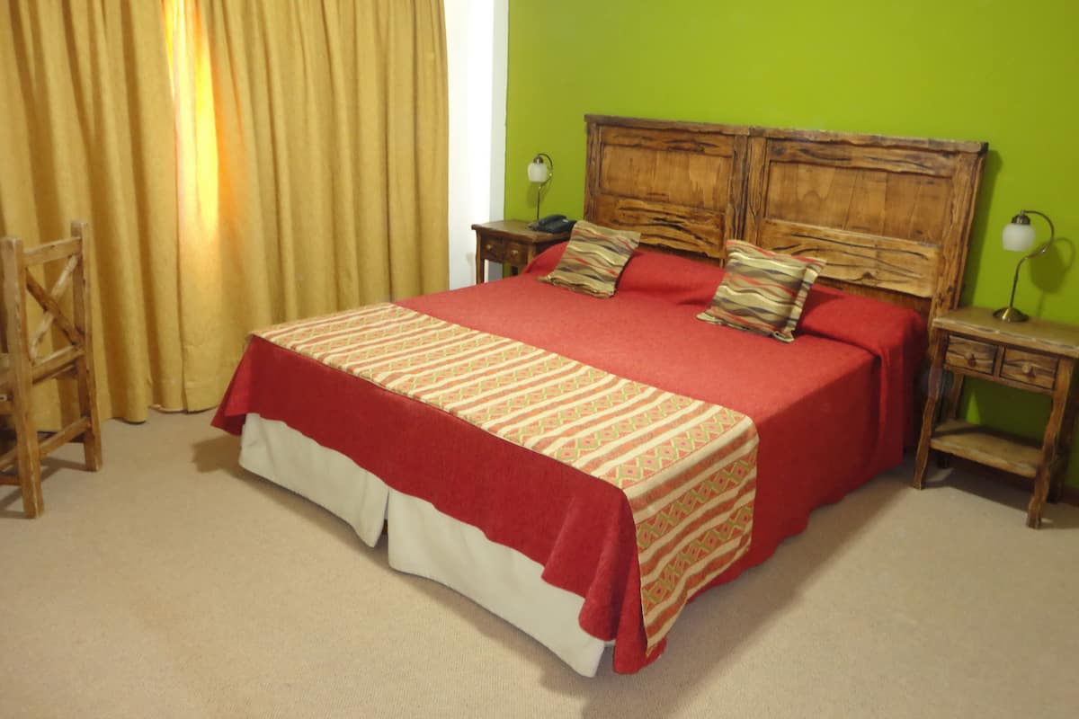 A bedroom with a large bed, wooden headboard, two bedside tables, a chair, and a green wall.