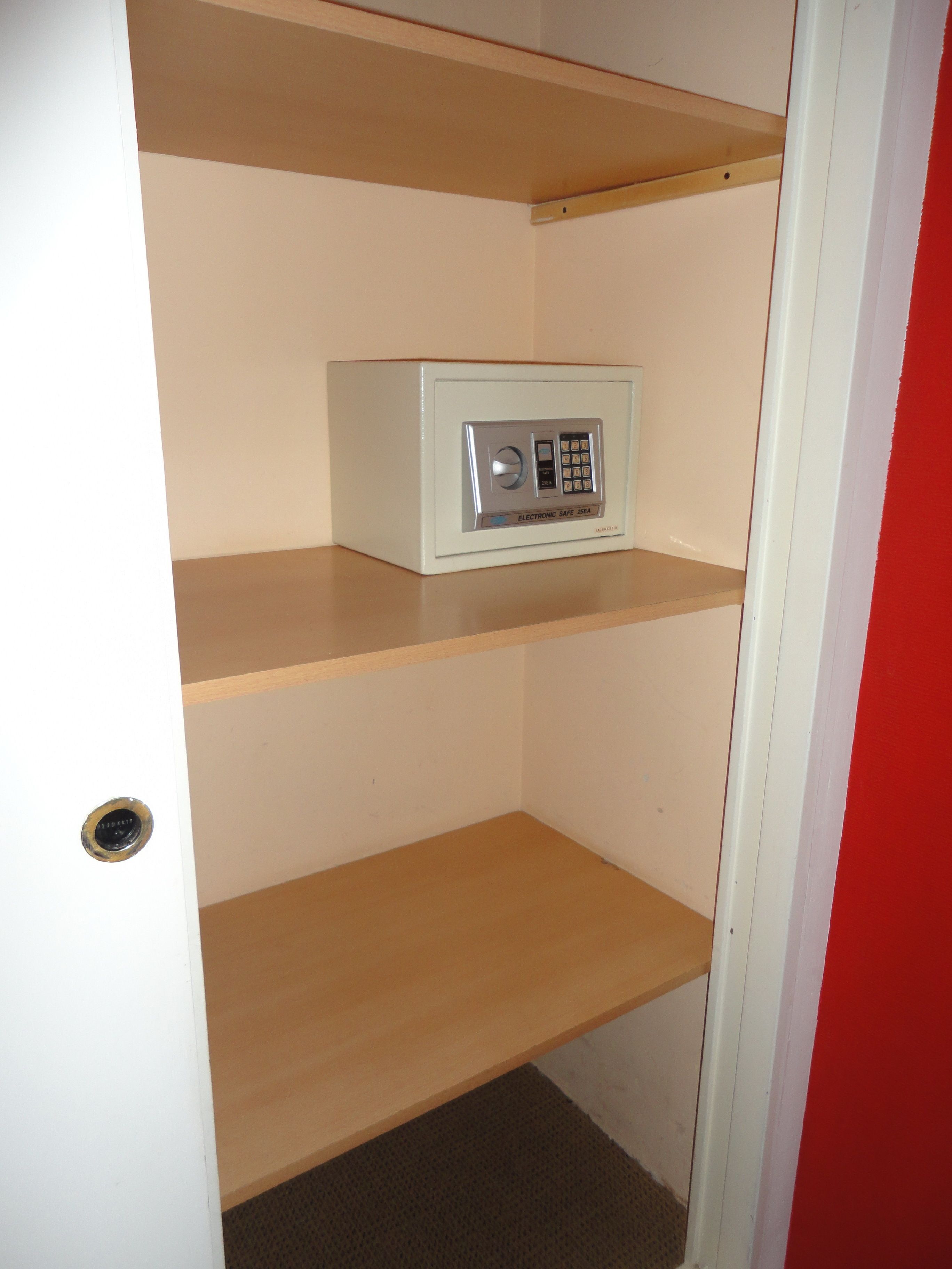 Una habitación con una caja fuerte blanca en la repisa superior y una puerta con pomo redondeado.