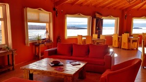 A cozy living room with a red sofa, a wooden coffee table, and a view of the sea. - Aikendor Hotel Panorámico (El Calafate)