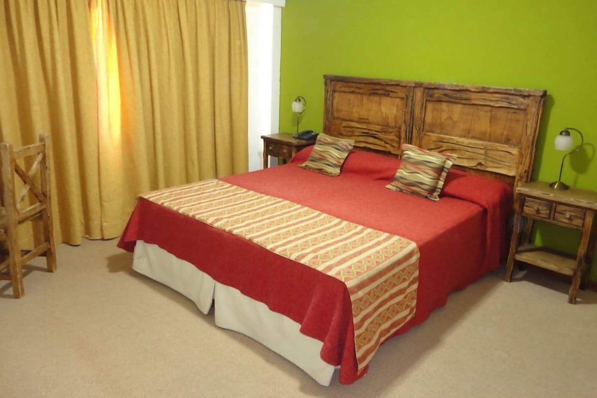 A bedroom with a large bed, wooden headboard, two bedside tables, and a chair.