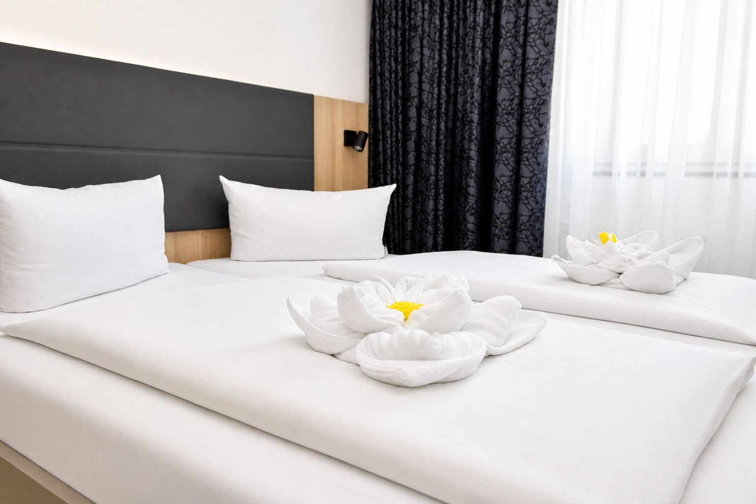 Habitación de hotel con cama, dos almohadas, cabecera y ventana con cortinas.