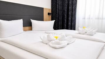 Habitación de hotel con cama, dos almohadas, cabecera y ventana con cortinas.