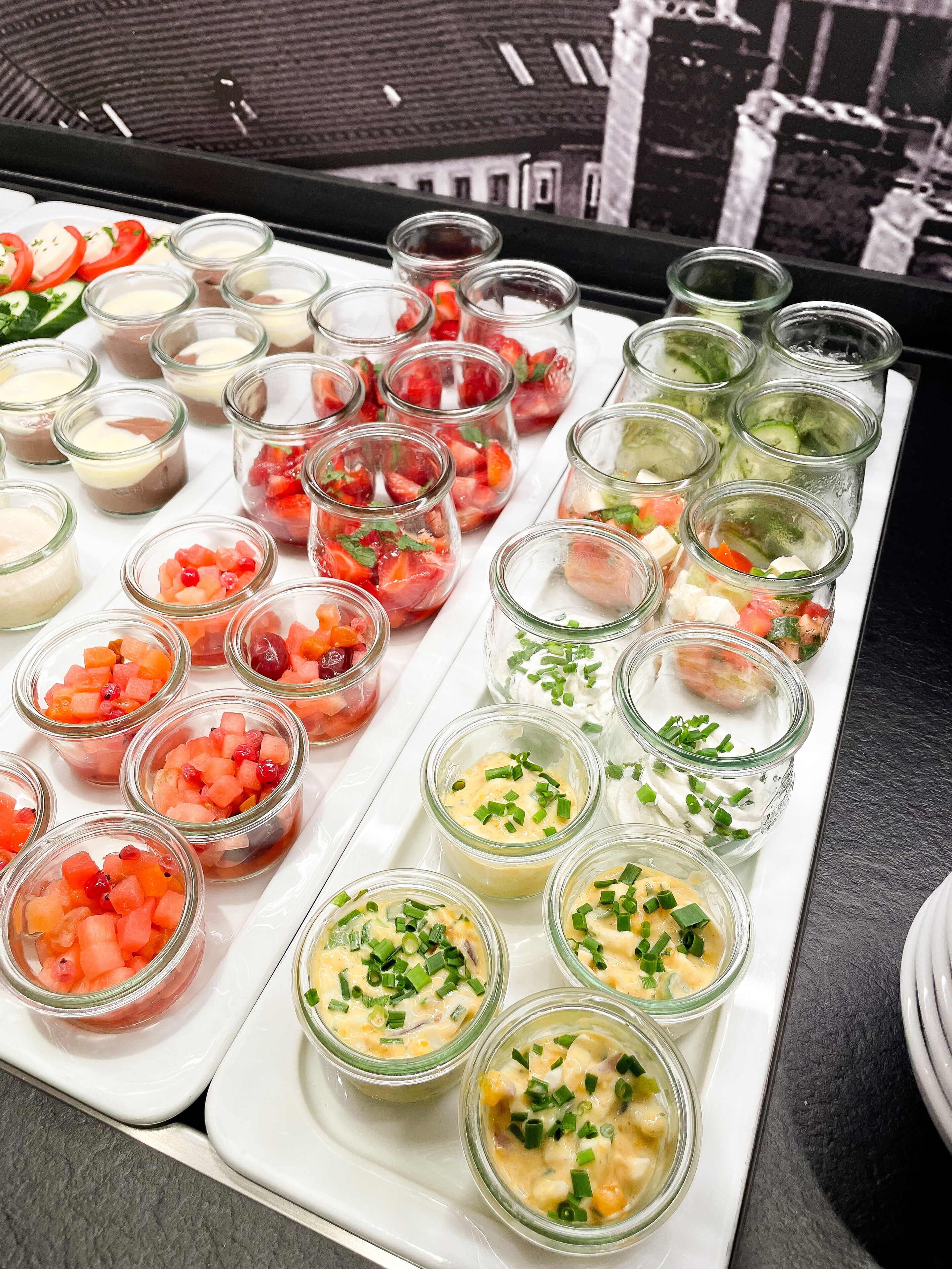 A tray of various food items, including fruit salads and creamy dishes, arranged on a white tray.
