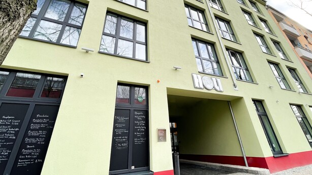 Ein mehrstöckiges Gebäude mit grüner Fassade, zahlreichen Fenstern und einem gut sichtbaren Eingang.