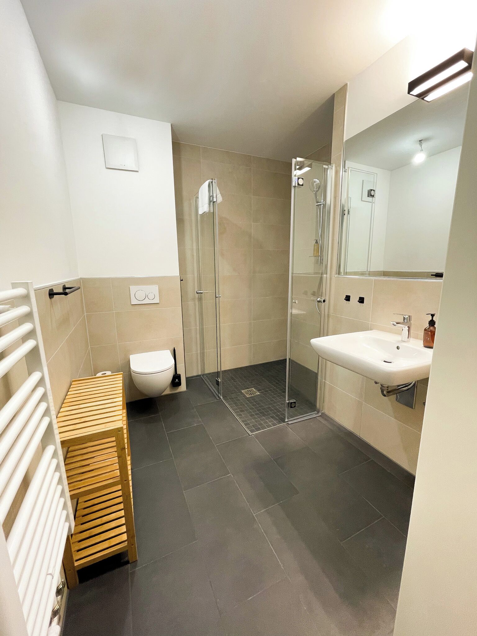 Un baño moderno con cabina de ducha de vidrio, un lavamanos blanco y un banco de madera.