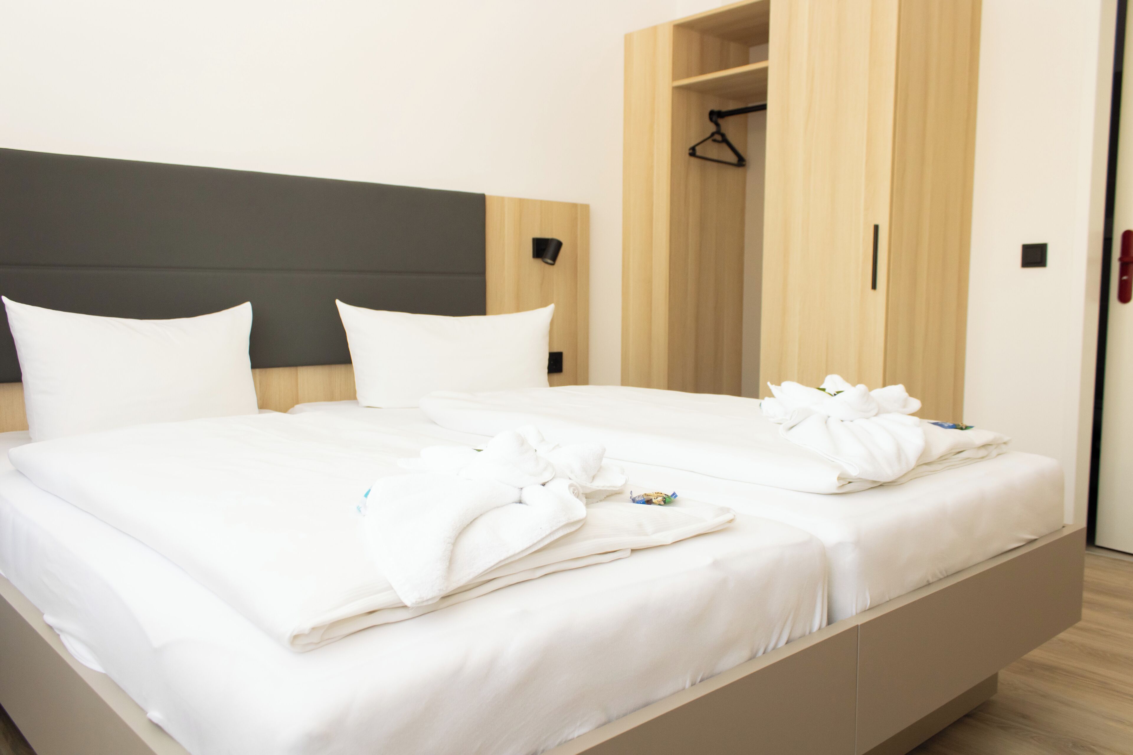 A modern hotel room with a large bed, wooden headboard, and a built-in wardrobe.