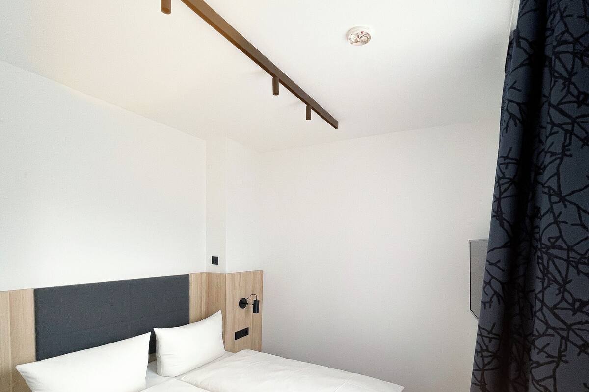A modern bedroom with a wooden headboard, a bed with white linens, a bedside table, and a nightstand.