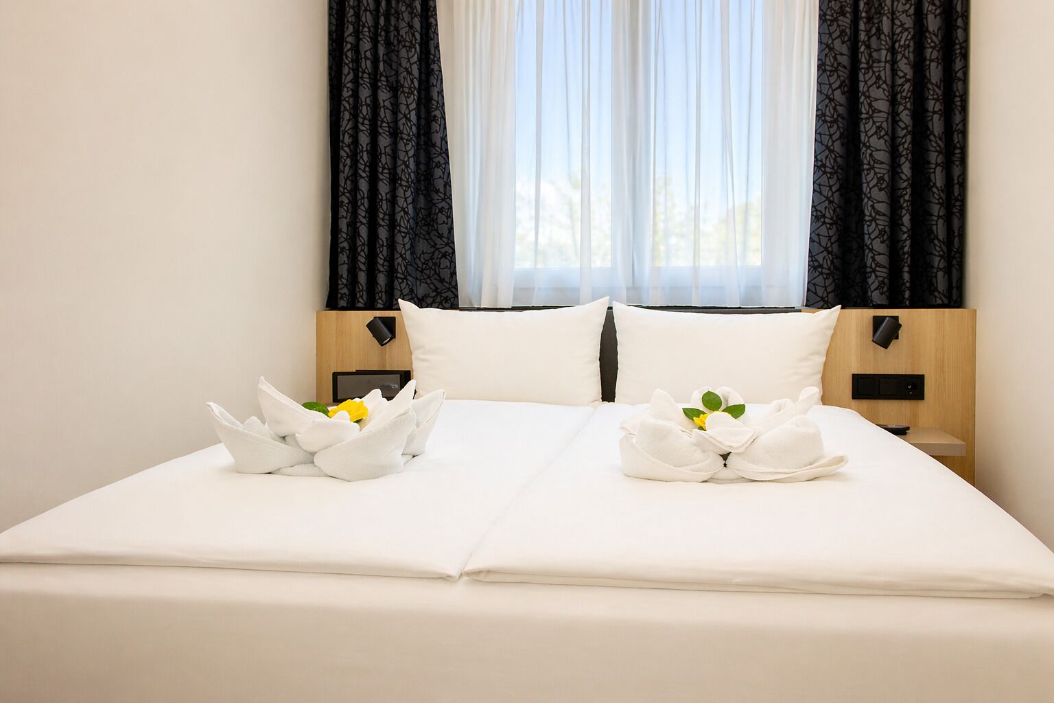 A neatly made bed with white linens, two pillows, and two decorative swans with flowers.