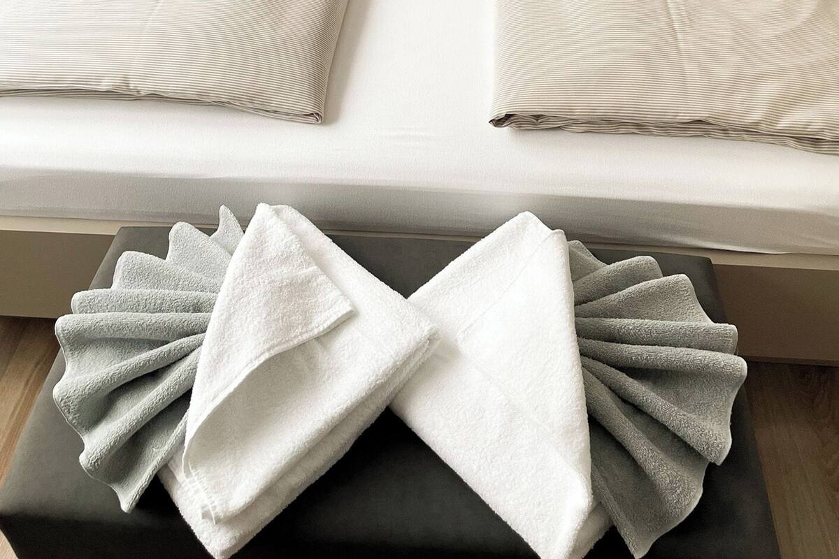 A double bed with a grey headboard and two pillows, a bedside table, and a folded towel on the floor.
