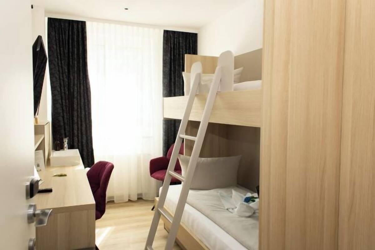 A bunk bed room with a desk and chair, a ladder, and a window with curtains.